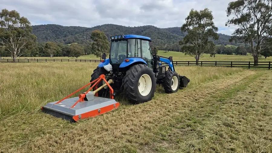 Tractor slashing a paddock, fresh-cut strips against taller grass.